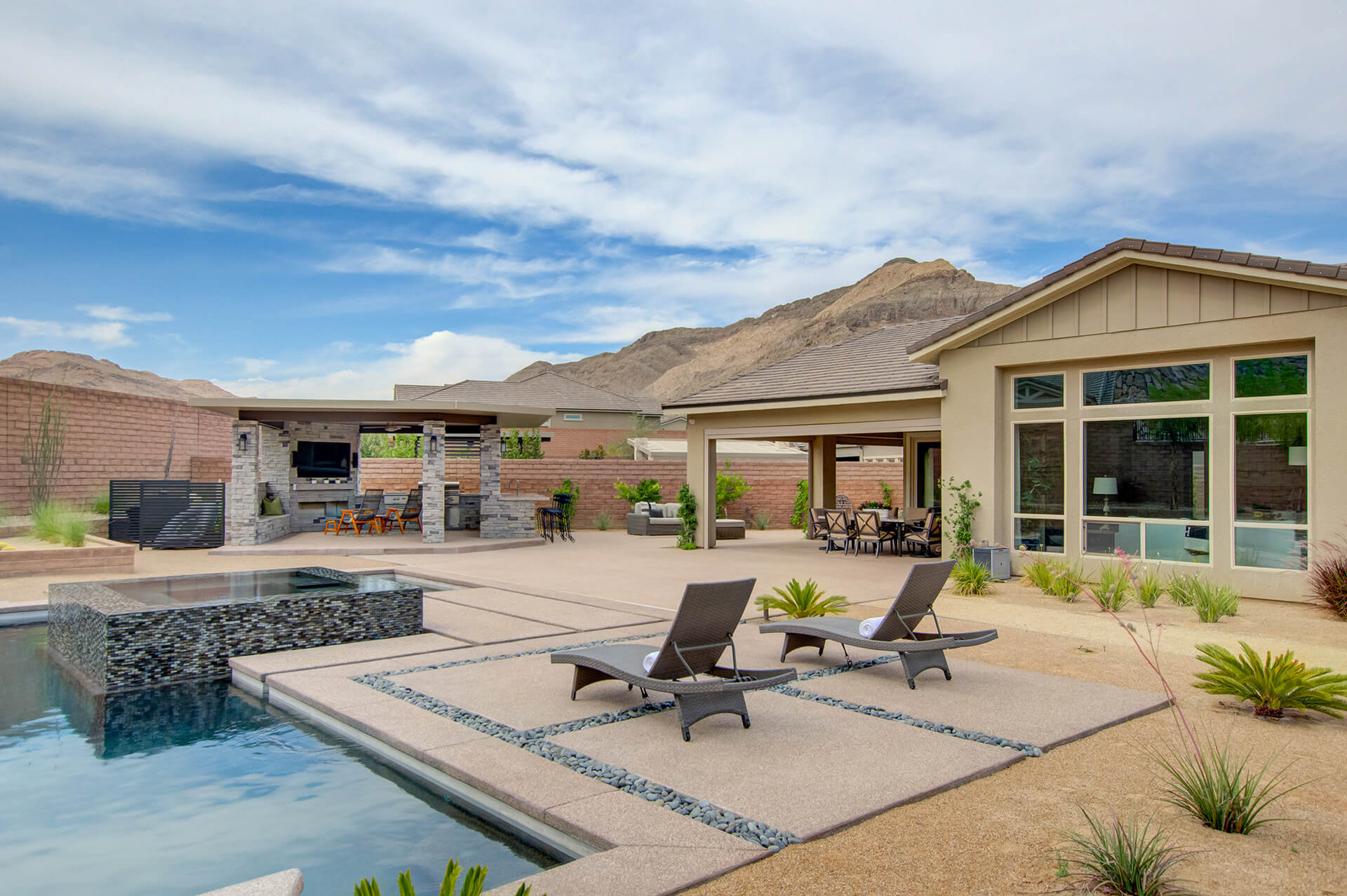 A pool with two lounge chairs and an outdoor kitchen.