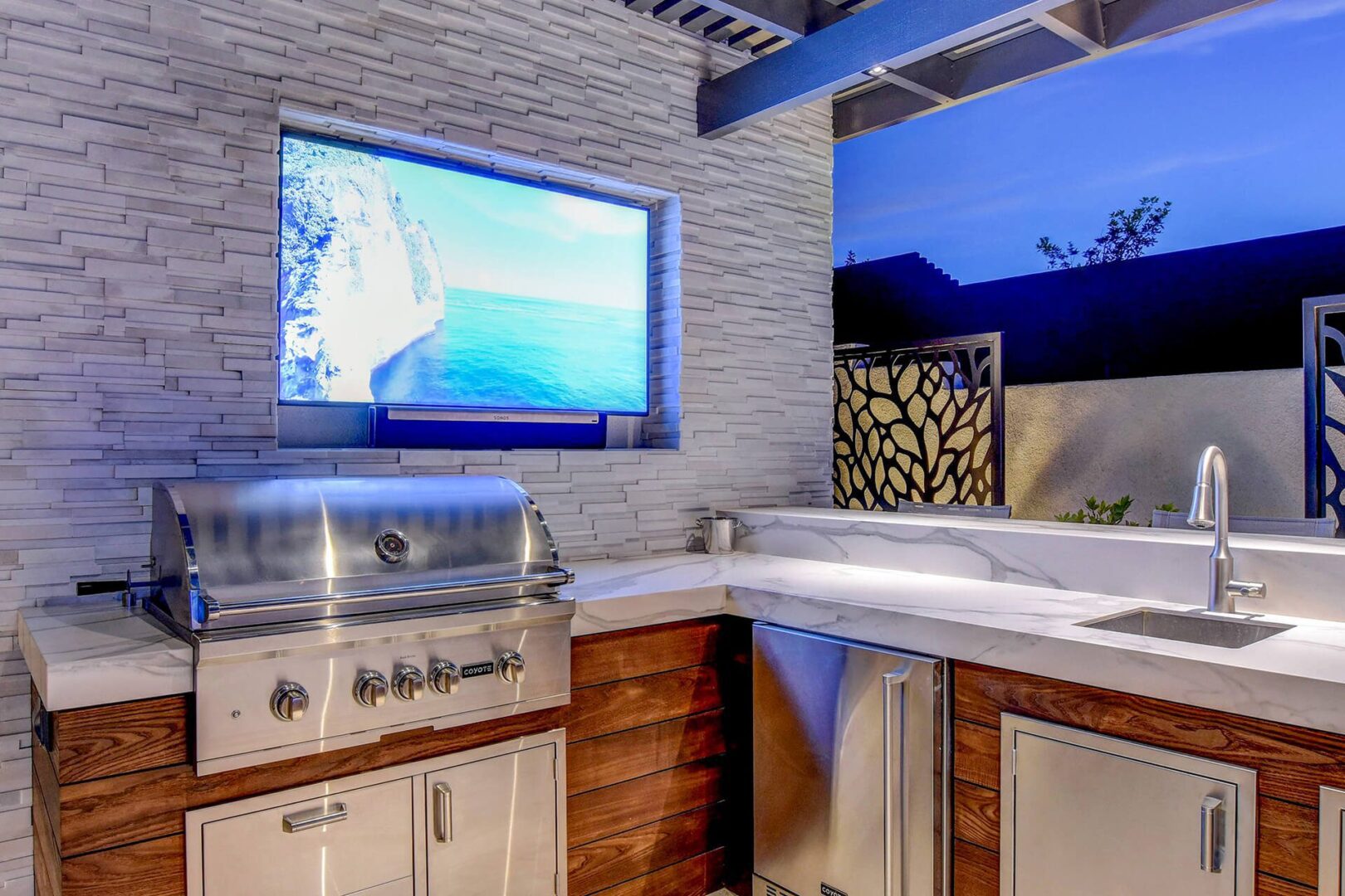 Thermory T&G Ash Cladding used to finish the outdoor kitchen cabinetry, paired with stacked stone finished media wall with recessed TV area