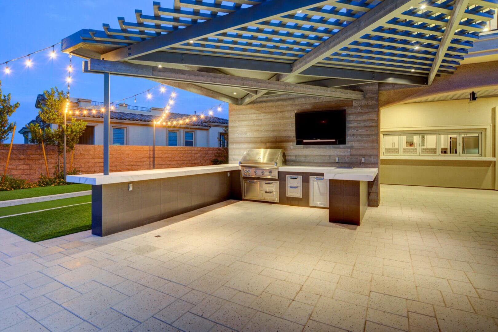 A man cleaning the metal tray of an outdoor grill placed on a small concrete counter next to a wooden fence.