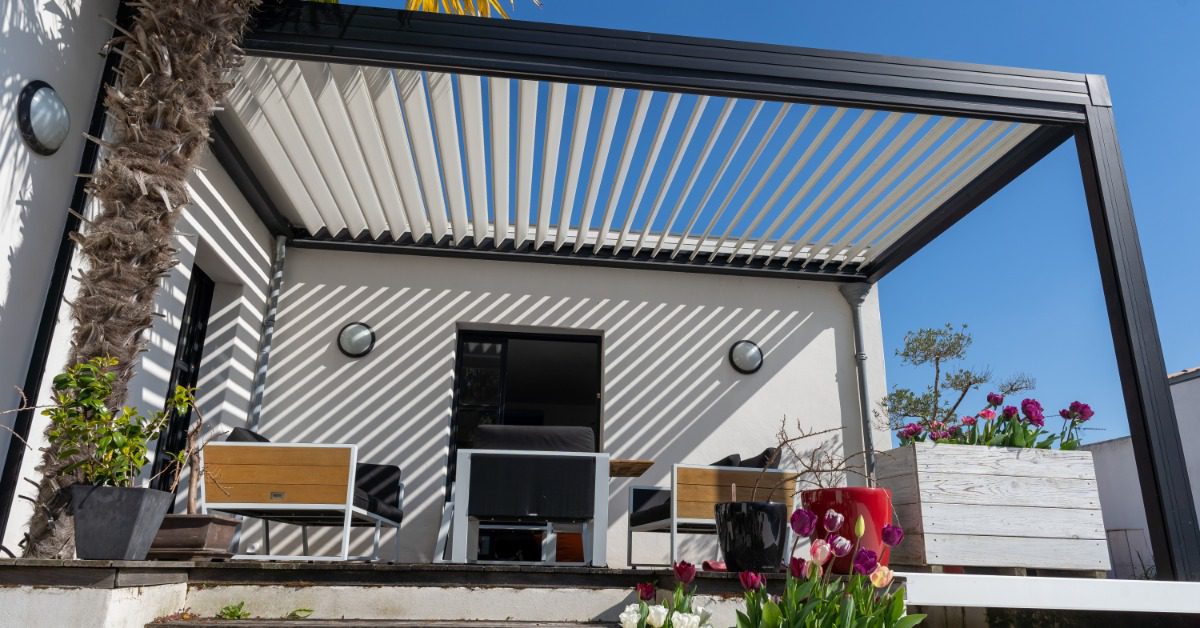 An aluminum patio cover on top of a small deck with wooden floors, chairs, a table, and multiple potted tulips.