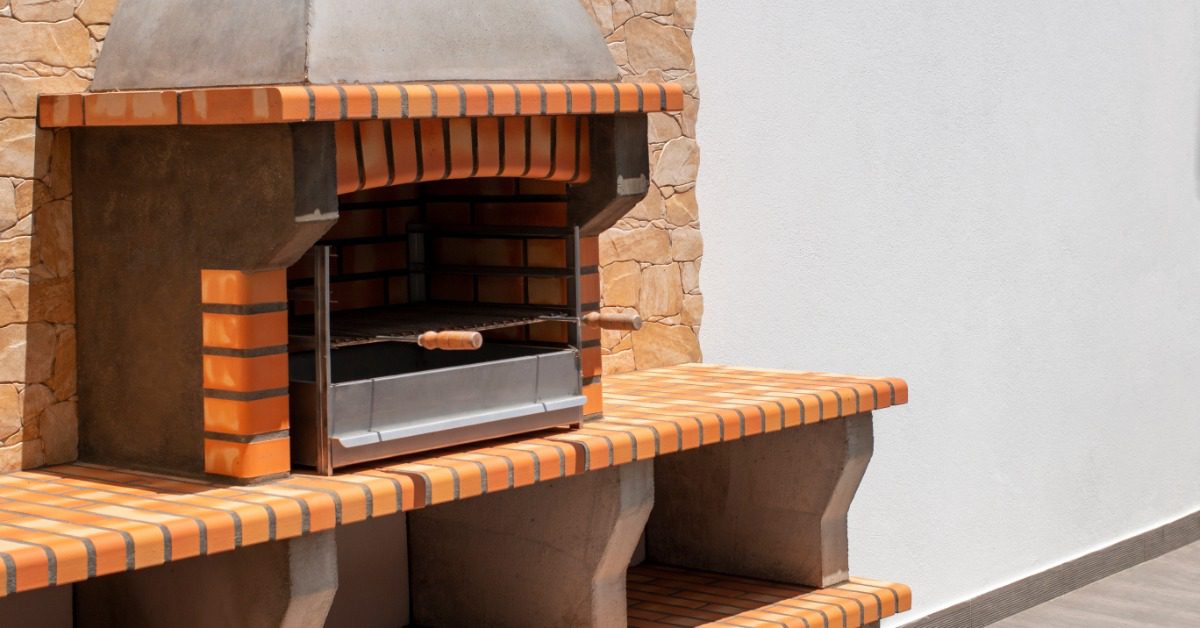 A brick and clay grill with multiple levels and storage compartments placed next to a tall white wall outdoors.