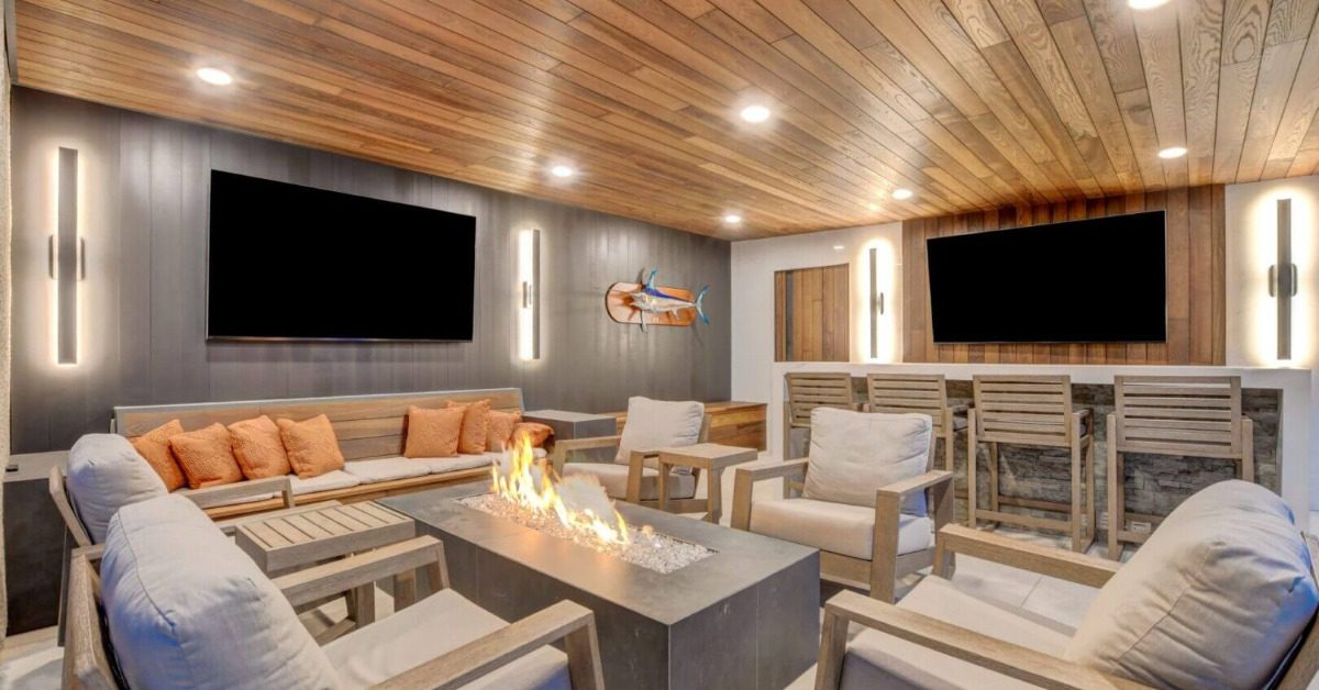 A close-up of a big flame in the center of a fire pit with a woman and a man sitting in the background with drinks.