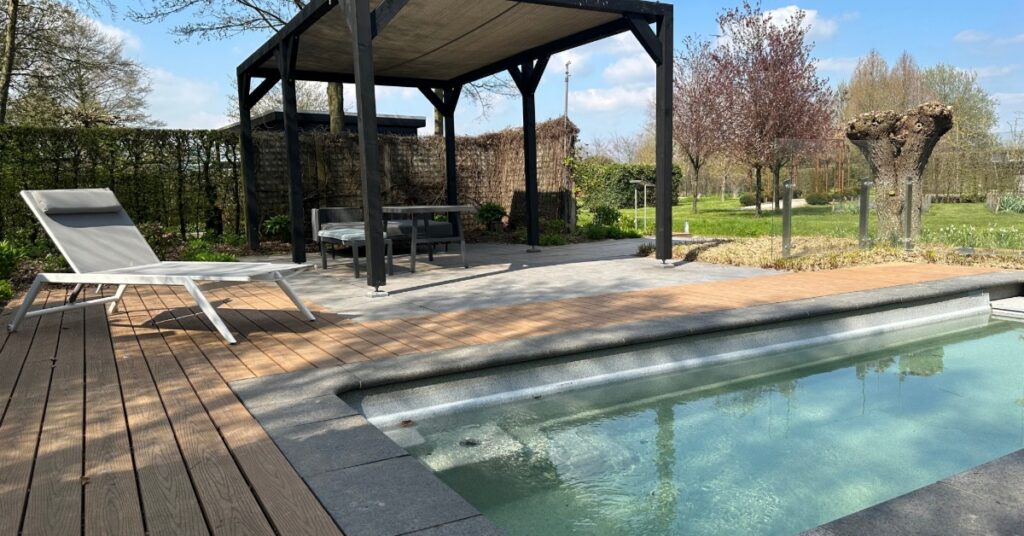 A pergola with six legs and a closed cover over a table and an outdoor couch, placed on a concrete base next to a pool.