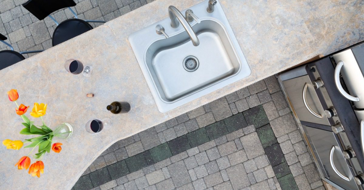 An aerial view of an outdoor stainless steel sink, placed on a granite counter, next to a stainless-steel grill.