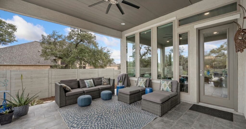 An outdoor patio with three couches, an area rug, and grey tile floors, under a roof with a ceiling fan and lights.