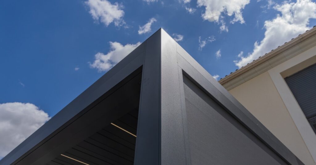 A close-up of the corner of a black aluminum pergola with multiple panels attached to the side of a two-story home.