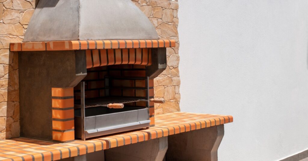 A close-up of a brick oven with three storage compartments placed next to a large white wall under the sun.
