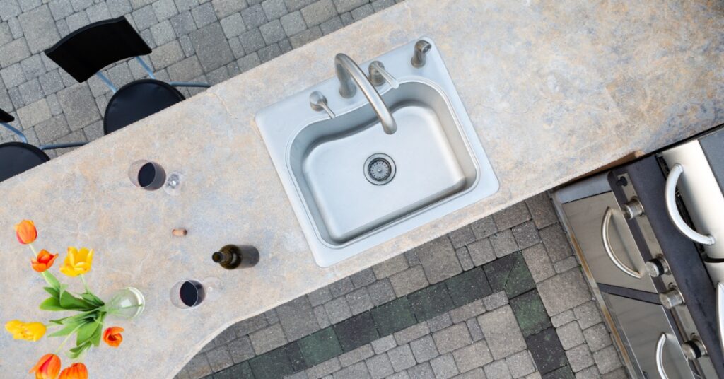 An aerial view of an outdoor countertop with a large sink and two wine glasses next to a stainless-steel grill.