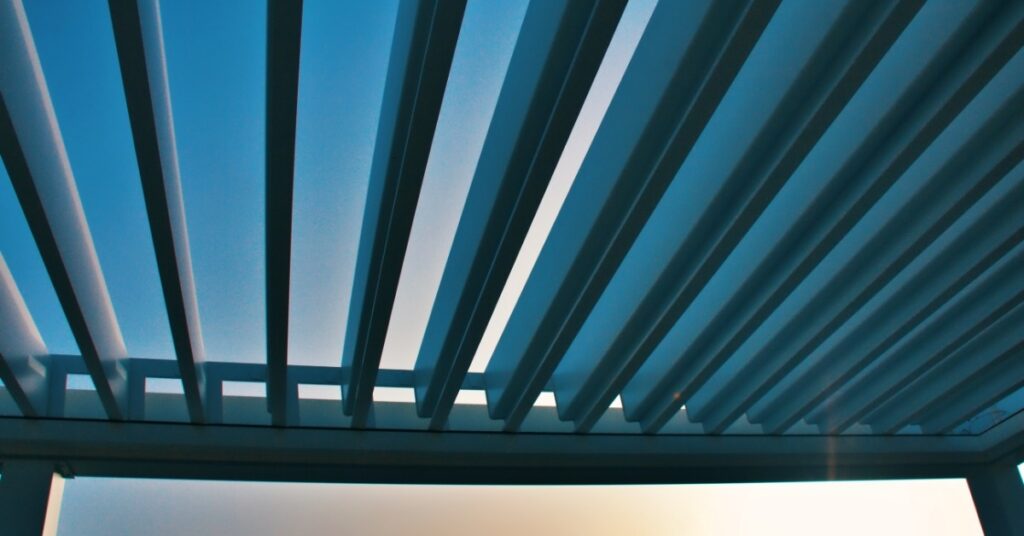 A close-up of the top moving panels of an aluminum pergola during a sunset with mountains in the background.