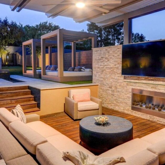 A man wearing a black apron, touching the cover of a stainless-steel grill, using a metal fork to flip a piece of meat.