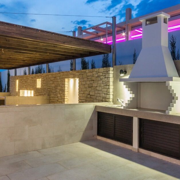 An outdoor kitchen with marble floors, a stove with a large chimney, and a counter next to a large sitting area.