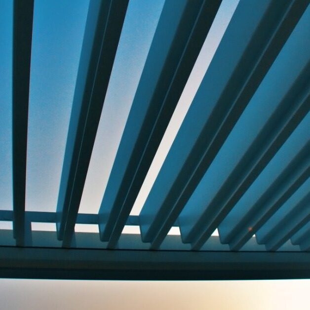 A close-up of the top moving panels of an aluminum pergola during a sunset with mountains in the background.